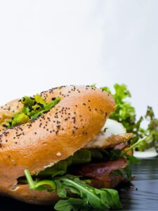 Close-up of a breakfast bagel sandwich filled with arugula and crispy bacon.