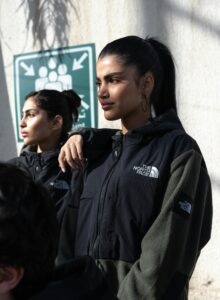 Two women in The North Face jackets standing outdoors under sunlight.