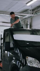 A man cleans the roof of a black van in an industrial indoor setting, focusing on maintenance.
