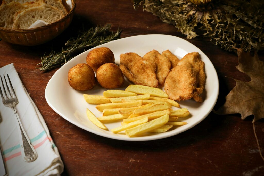 Plate of breaded chicken, French fries, and croquettes served on a wooden table.