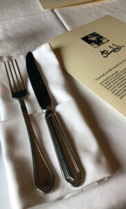 Elegant table setting with fork, knife, and Pandel menu on white tablecloth. Perfect for dining themes.