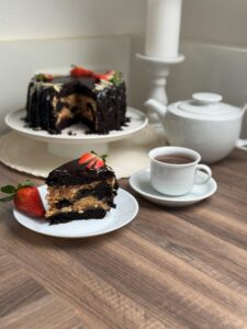 A slice of chocolate cake with strawberries next to a teapot and cup on a cozy table.