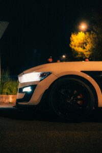 Close-up of a white sports car with headlights on in a night setting.
