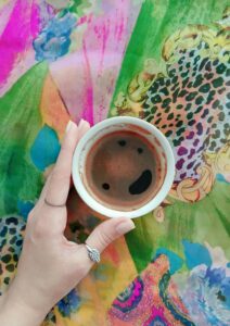 A hand holding a coffee cup over a lively, multicolored fabric with leopard print and floral designs.