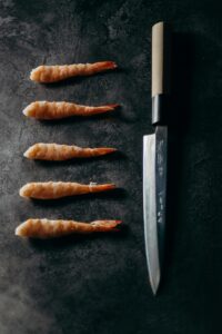 Top view of raw shrimp elegantly arranged with a sharp knife on a dark background, showcasing food art.