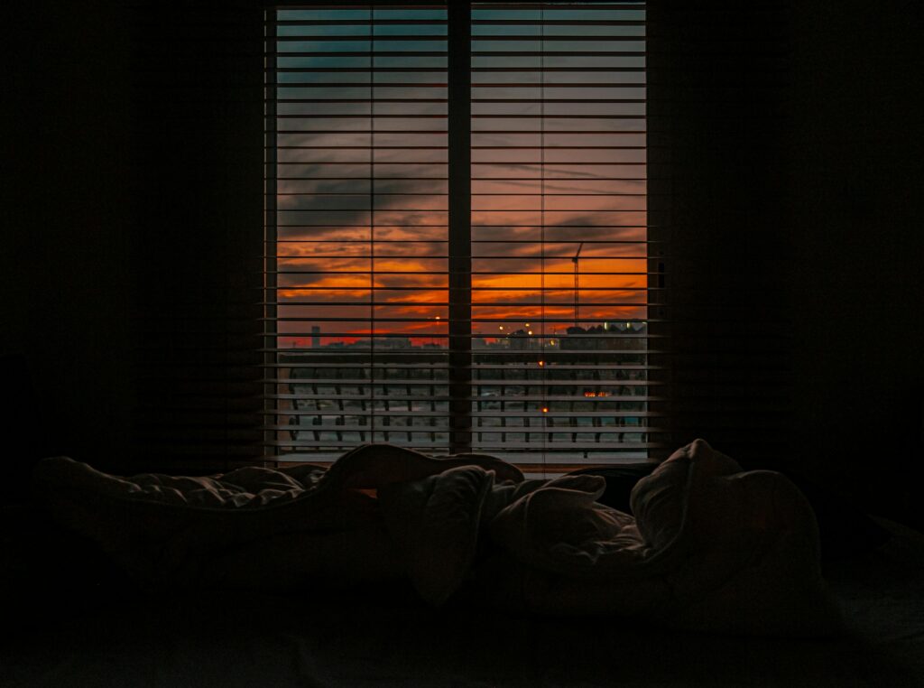 Cozy bedroom with a view of a vibrant sunset through window blinds.