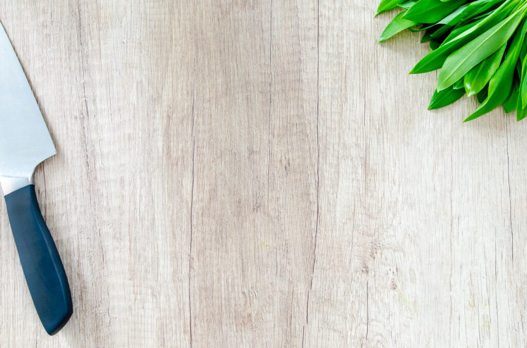 Fresh herbs and a chef knife on a wooden surface with copy space.