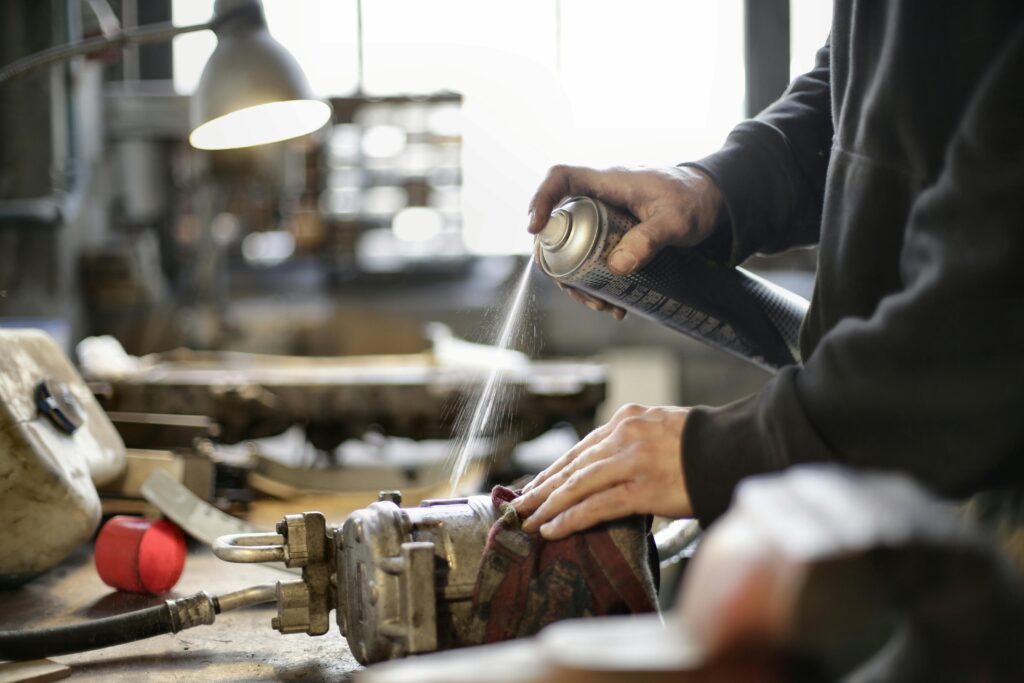 Person cleaning machine part with spray can in workshop environment.