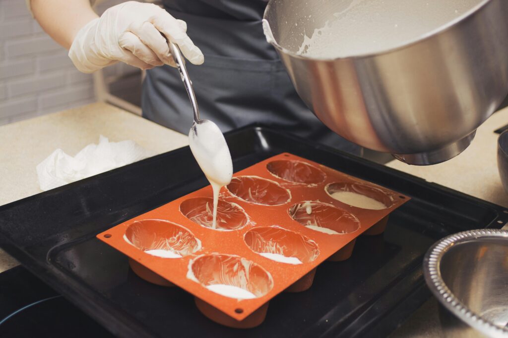 Chef wearing gloves pours batter into silicone molds, preparing for baking.