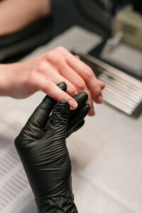 A professional manicurist wearing black gloves provides a manicure service to a client.