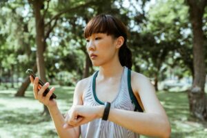 Young woman in sportswear checking her smart watch and smartphone in a sunny park.