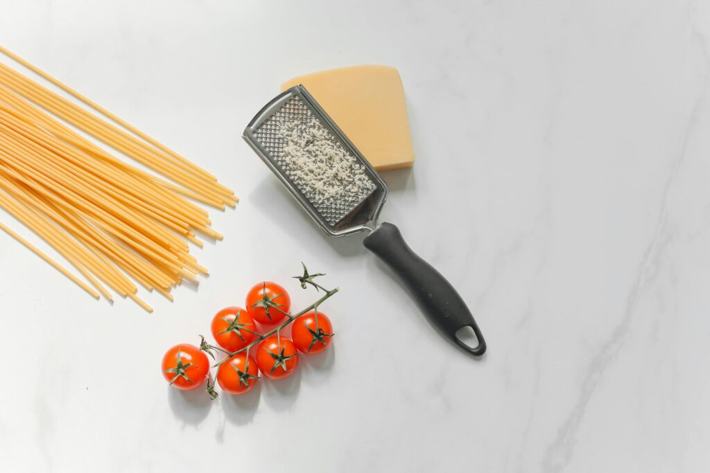 Flat lay image of pasta ingredients including spaghetti, parmesan cheese, tomatoes, and a grater.
