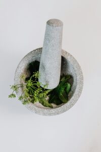 Top view of a stone mortar and pestle grinding fresh green herbs on a white background.
