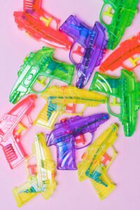 Bright multicolored toy water guns on pink background ideal for play or leisure themes.