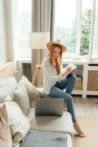 Young woman enjoying remote work lifestyle, writing notes beside a laptop in a stylish home setting.