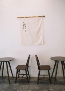 A serene minimalist interior featuring wooden chairs and tables with a fabric sign on the wall.
