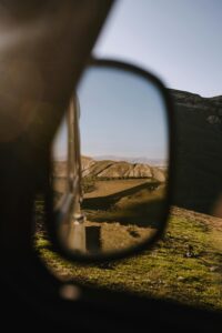 Reflection of mountainous landscape in car side mirror under clear skies.
