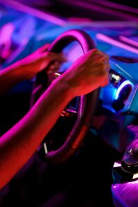 Person holding a steering wheel in an illuminated gaming arcade setting.