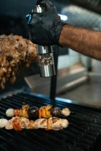 Chef seasoning skewers with bell peppers and mushrooms on grill, showcasing culinary precision.
