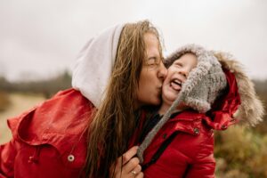 A joyful moment of a mother kissing her child in the rain, both wearing red jackets.