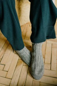Woolen knitted socks over black pants on a wooden parquet floor.