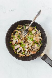 Delicious sautéed mushrooms and onions in a frying pan for a tasty meal.