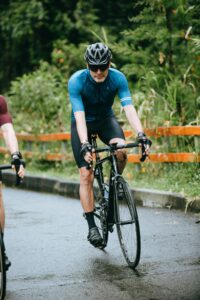 A cyclist wearing sports gear rides along a wet road amid lush greenery, showcasing outdoor activity and fitness.