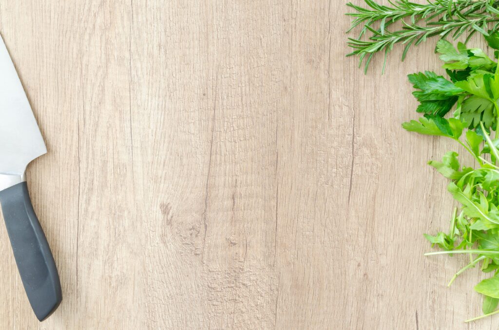 Top view of fresh rosemary and parsley with a chef's knife on a wooden surface, offering ample copyspace.