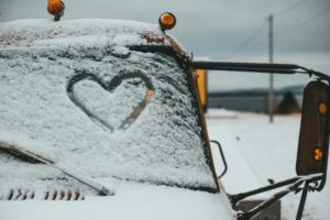 Finger drawn heart symbol on windshield of truck covered with hoarfrost parked on snowy terrain of waterside on winter day