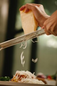 A hand grates fresh cheese onto a plate of spaghetti, highlighting culinary preparation.