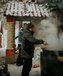 Man cooking outdoors in snowy Ust'-Kamenogorsk, Kazakhstan during winter.