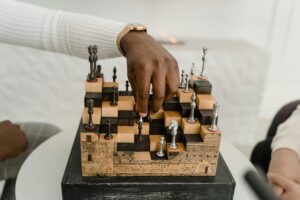 A close-up of a hand making a strategic move on a unique 3D chessboard indoors.