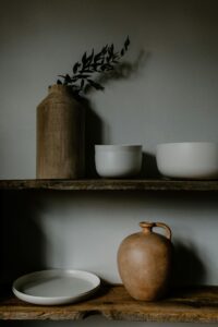 Minimalist display of ceramics and vases on rustic wooden shelves in neutral tones.