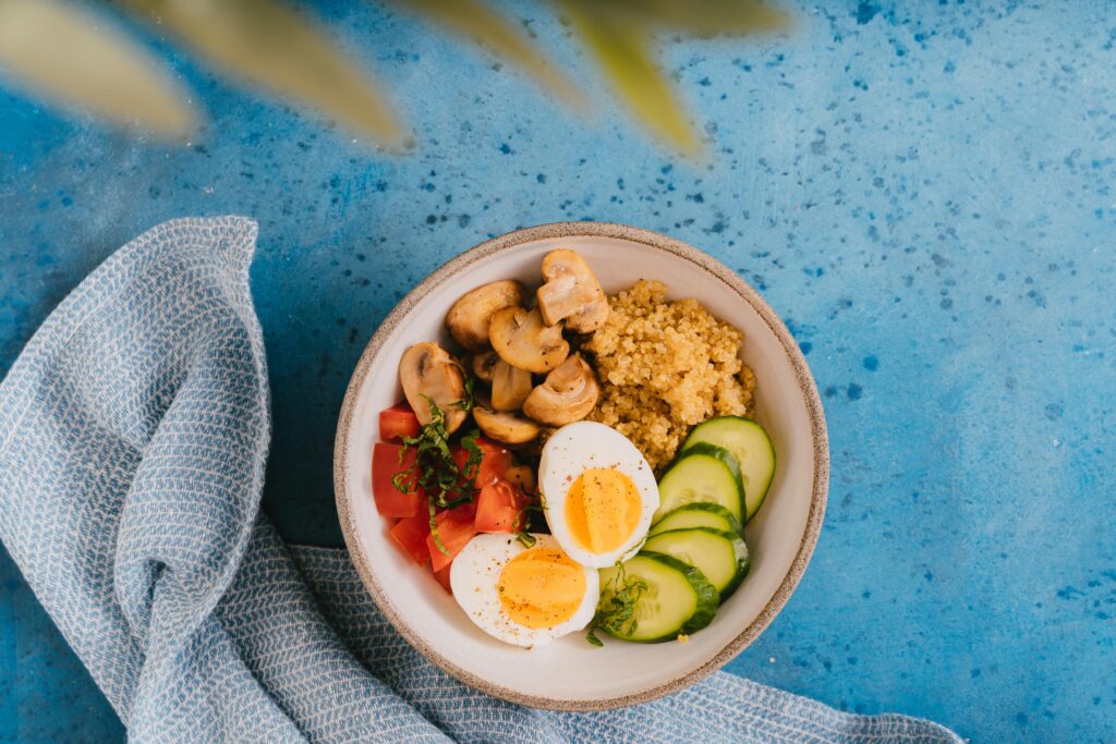 A delicious and healthy breakfast bowl featuring quinoa, boiled eggs, vegetables on a blue background.