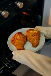 Close-up of fresh croissants on a plate being taken out of an oven with gloves.