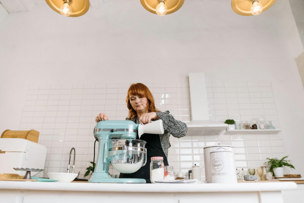 Woman pouring milk into a stand mixer while baking in a stylish kitchen.