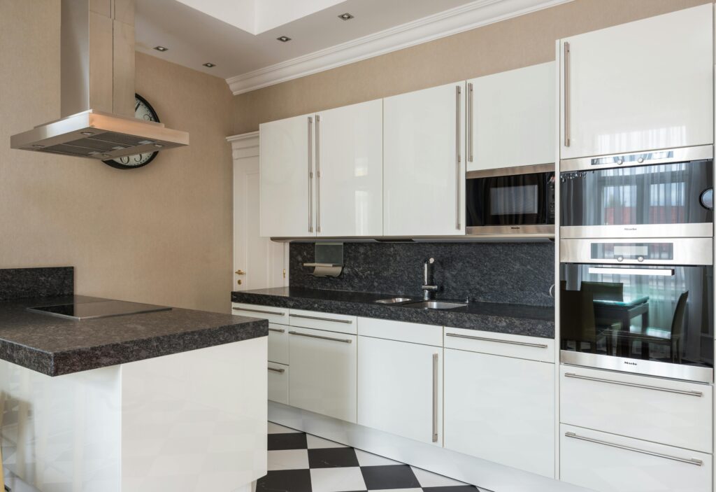 Interior of modern kitchen made in minimalist design with glossy cabinets and built in microwave oven and stove on counter under hood