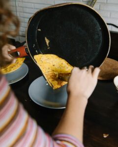 A person serves a freshly made omelette from a nonstick pan onto a plate.