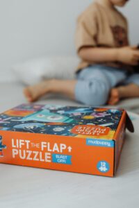 Close-up of a child near a lift-the-flap puzzle box on a bed.