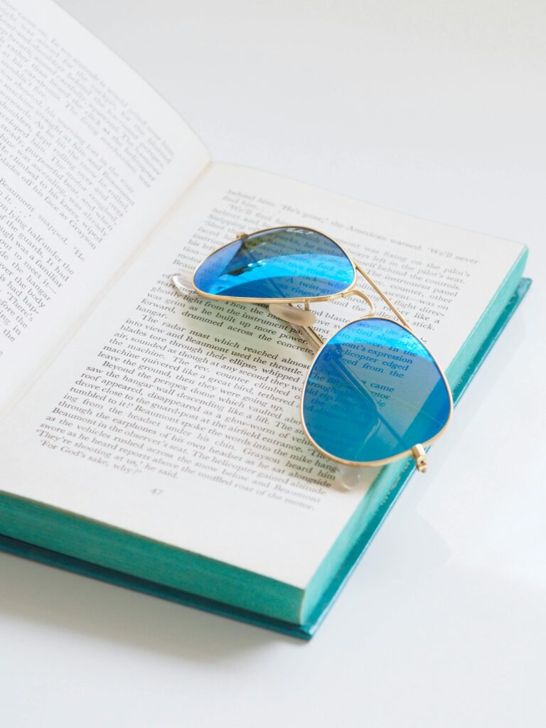 Blue sunglasses rest on an open book, highlighting a blend of fashion and literature.