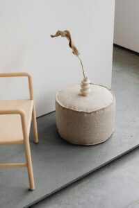 A stylish minimalist interior with a pouffe, chair, and decorative vase.