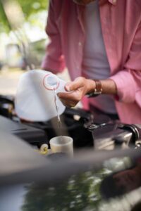 A man in a pink shirt pouring coolant into a car engine, highlighting vehicle maintenance.