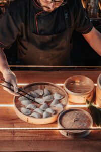 Close-up of a chef carefully cooking dumplings in a bamboo steamer tray, showcasing culinary expertise.