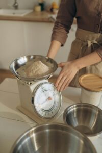 A woman weighing flour using a kitchen scale, preparing for baking in a cozy kitchen setting.