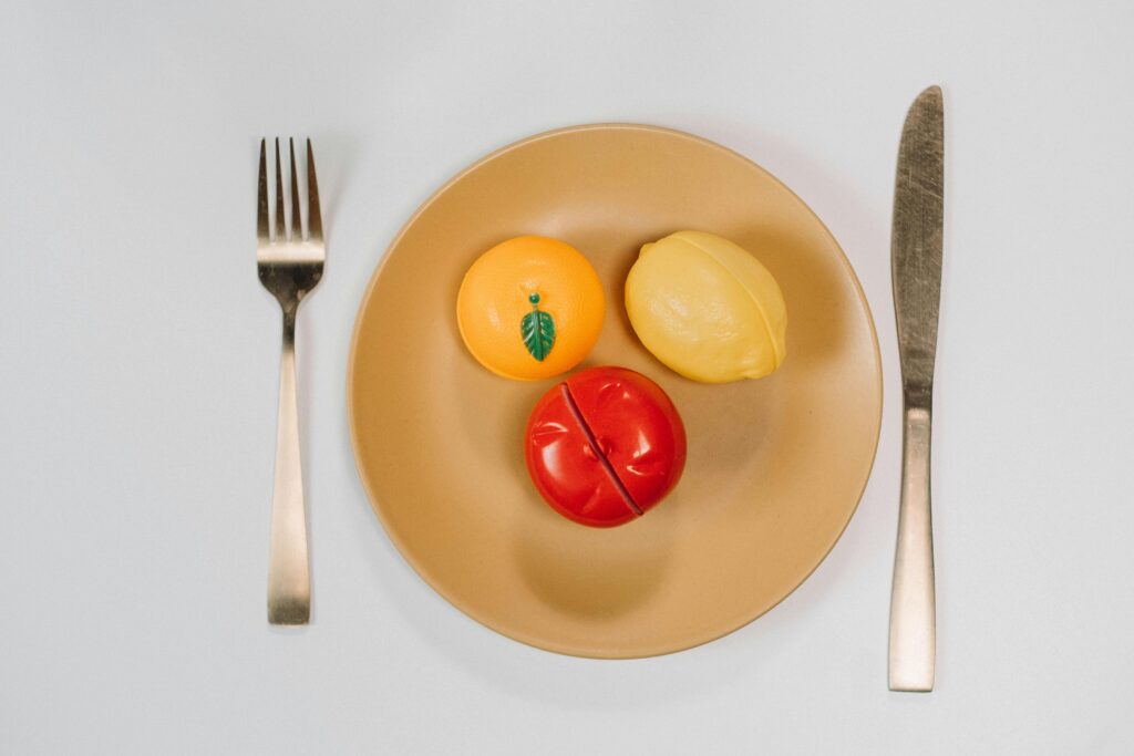 Colorful toy fruits on a plate with silverware in a conceptual flat lay arrangement.