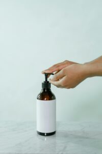 Close-up of hands pressing a soap pump bottle on a marble surface, offering copy space.