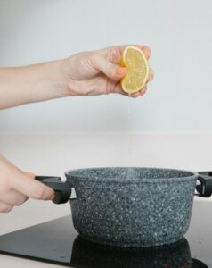 Fresh lemon juice being squeezed into a granite pot for cooking preparation.