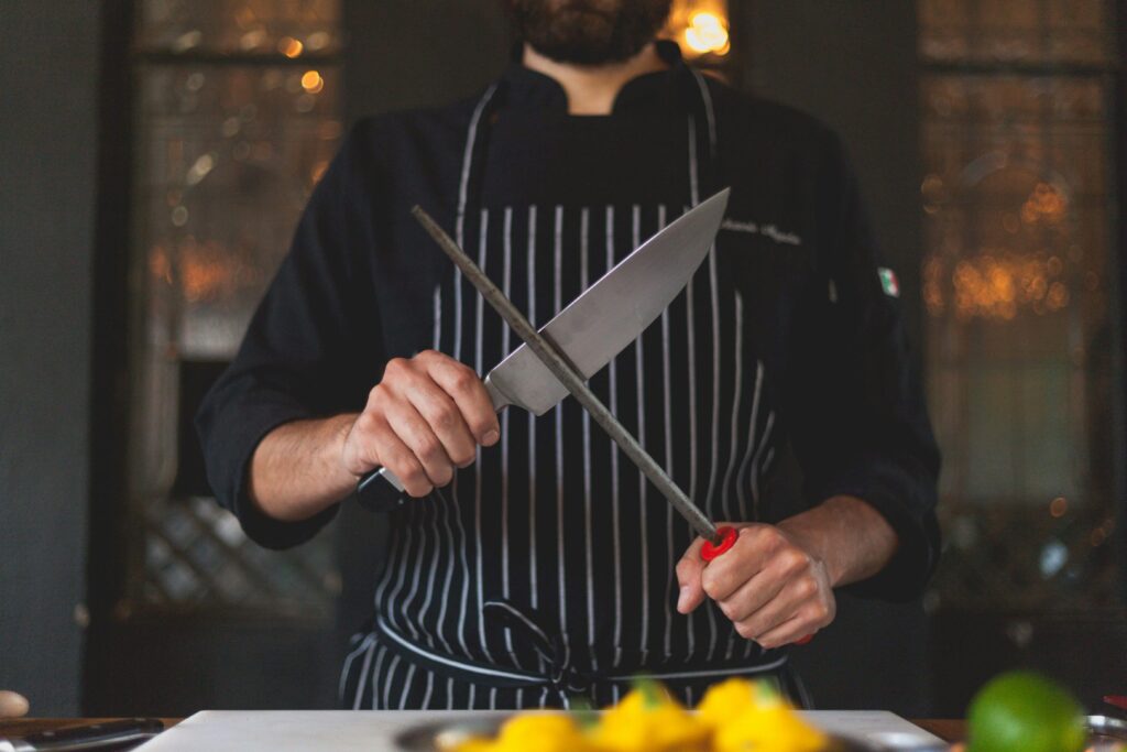 Chef sharpening a knife with a honing rod in a professional kitchen setting, focusing on precision and culinary skill.