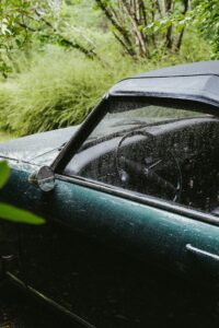 A detailed image of a vintage car covered in raindrops parked outdoors in a lush French landscape.