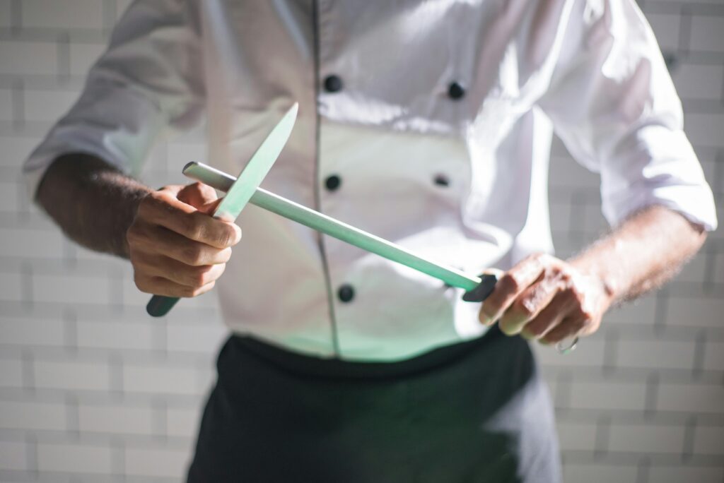 Close-up of a chef sharpening a knife with a honing rod in a modern kitchen setting.